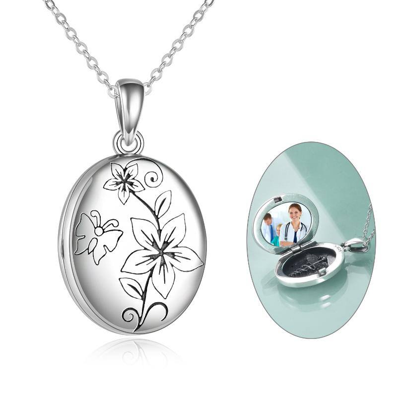 Oval silver locket pendant on a chain with a black floral engraving; opens to reveal a photo insert and mirror inside.