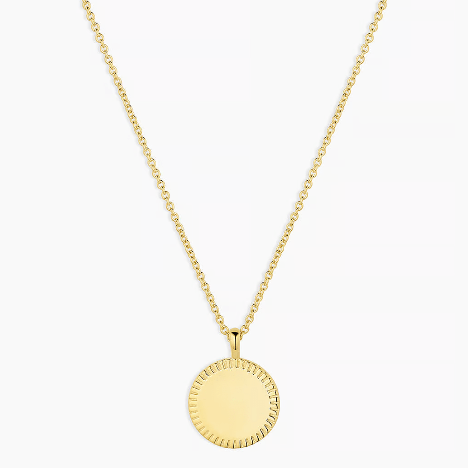 Gold chain necklace with a round, sunburst-edged pendant hanging center stage