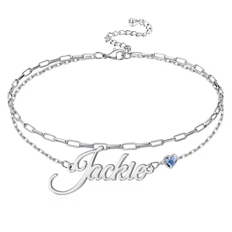 Silver name bracelet with the word 'Jackie' in script and a small blue heart charm, on an adjustable chain with a lobster clasp.