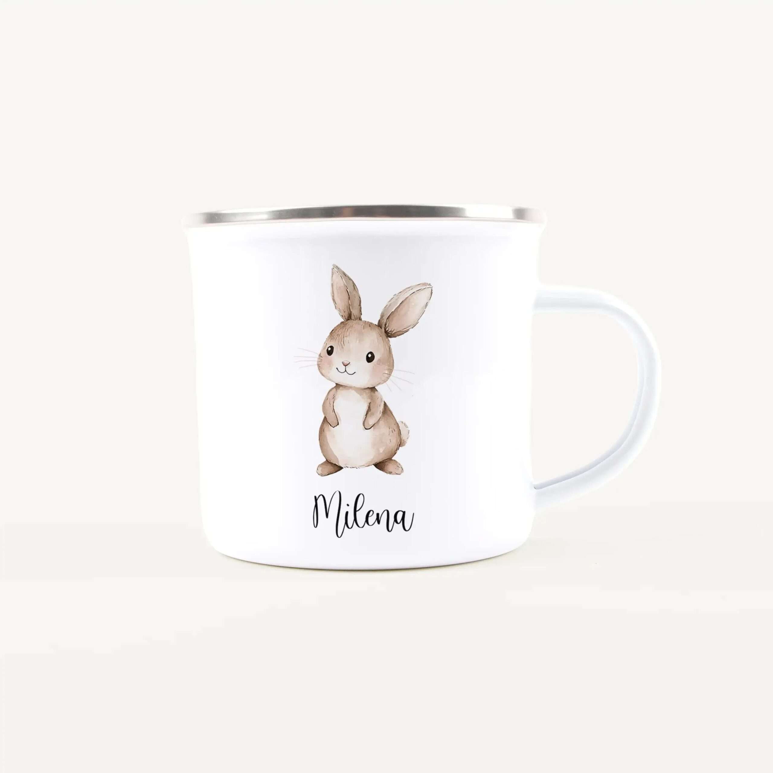 White ceramic mug with a silver rim, showing a vertical label featuring a cute watercolor bunny illustration and the name Milena.