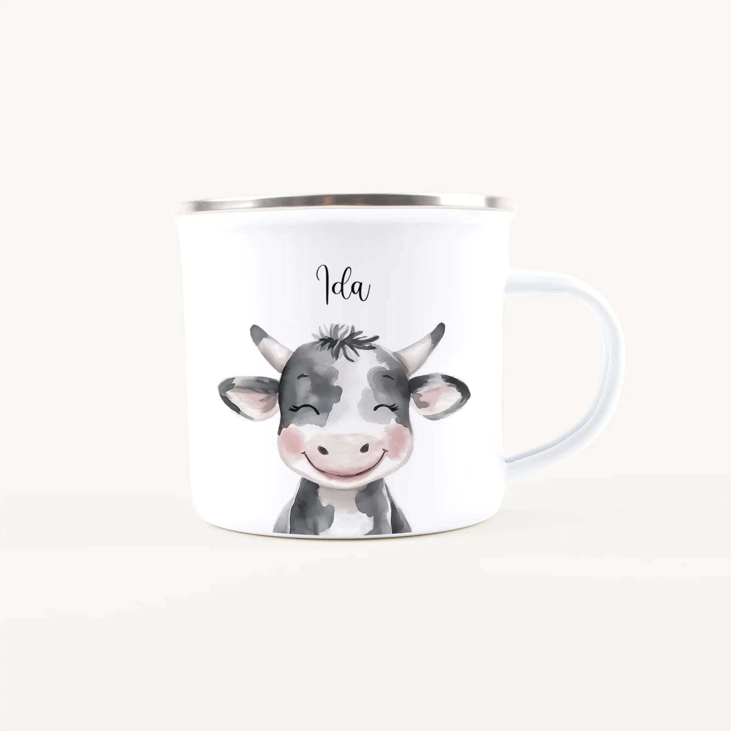 White ceramic mug with a silver rim featuring a cute cow illustration and the name Ida.