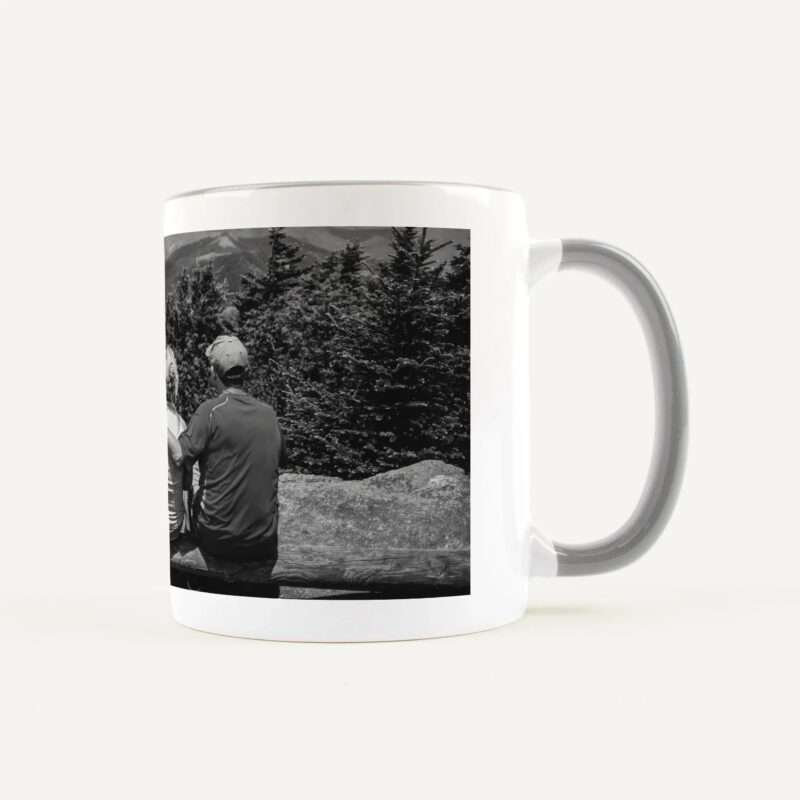 White ceramic mug with a black-and-white photo wrap showing hikers in a forested mountain landscape.