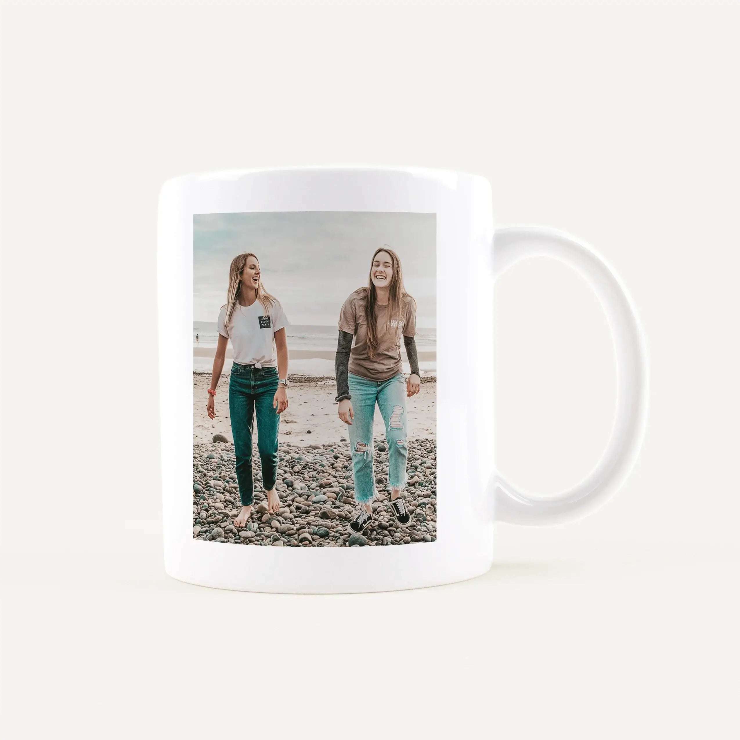Mug featuring a printed photo of three young women walking on a rocky beach.