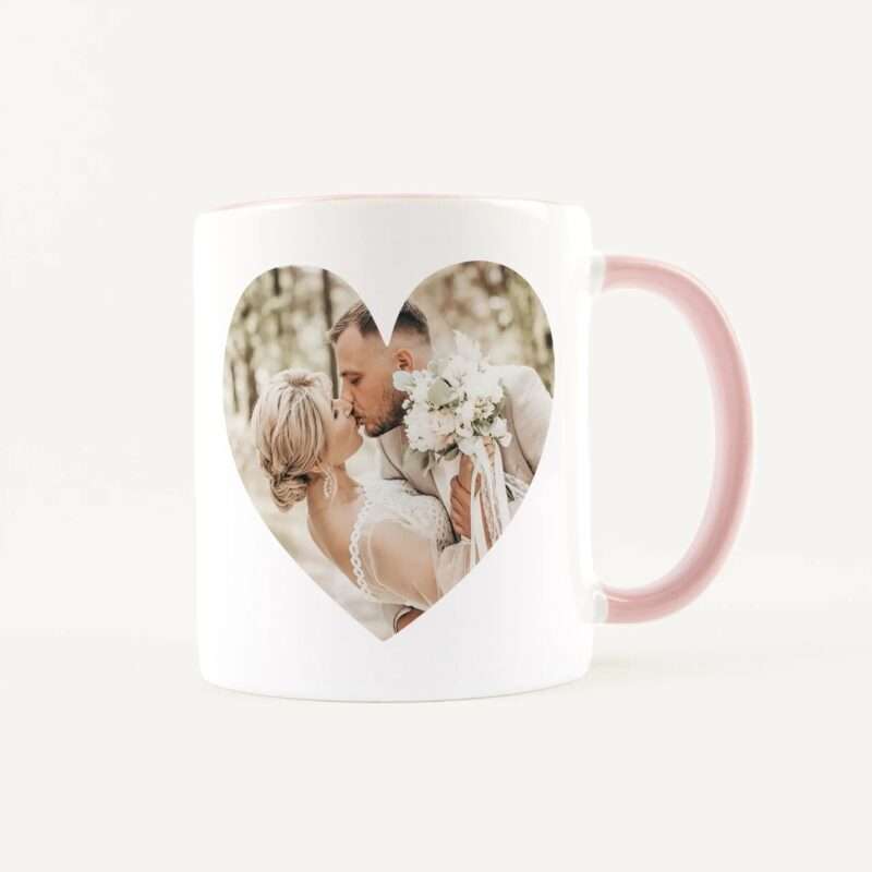 White mug with a pink handle featuring a heart-shaped window that reveals a wedding couple kissing inside the photo.