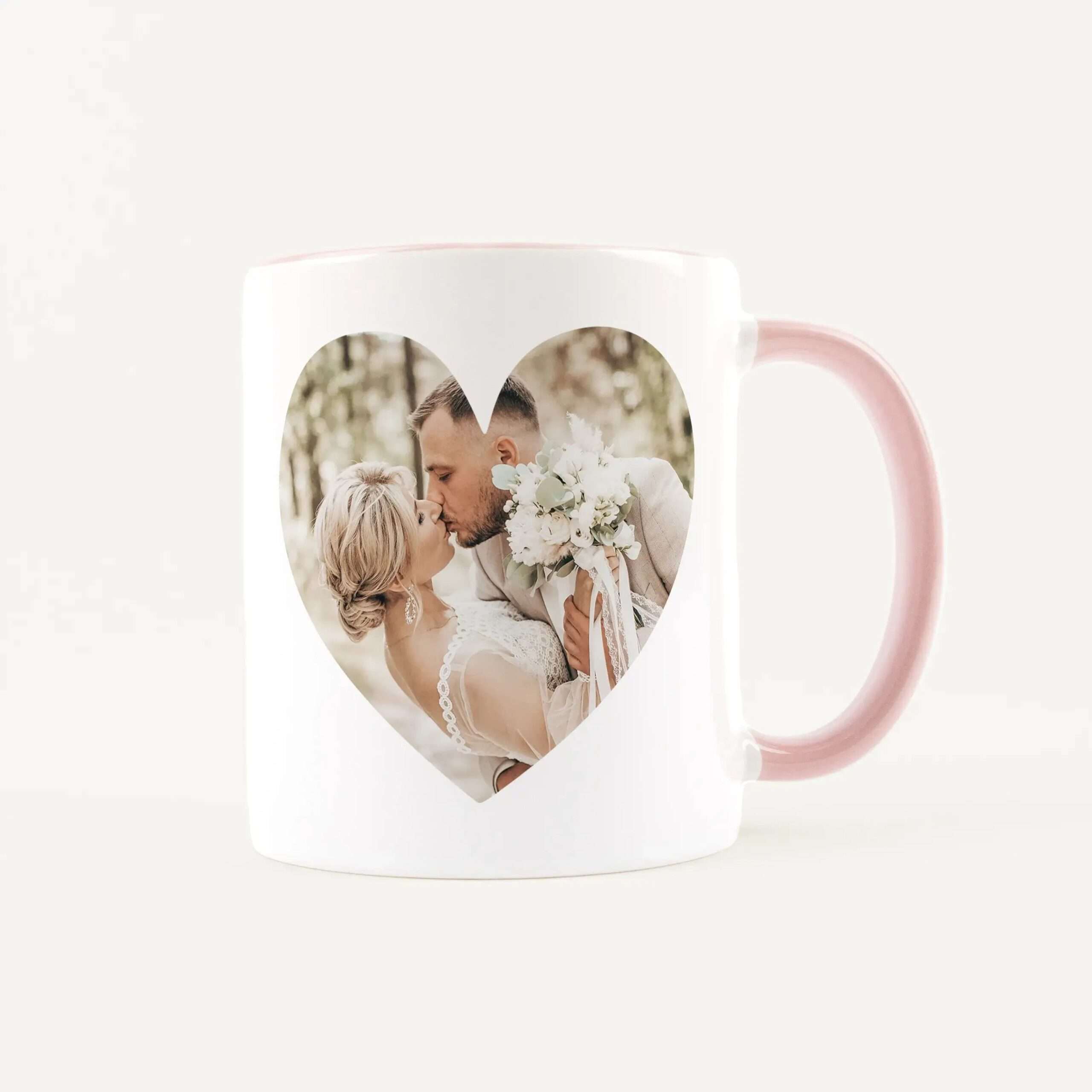 White mug with a pink handle featuring a heart-shaped window that reveals a wedding couple kissing inside the photo.