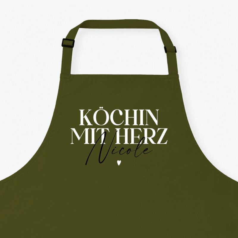 Olive-green apron with shoulder straps against a pale background and the German phrase 'Köchin mit Herz' in white lettering with a small heart.