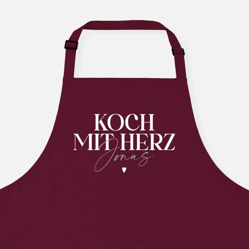 Maroon kitchen apron with adjustable straps, shown from chest down, text 'KOCH' visible on front.