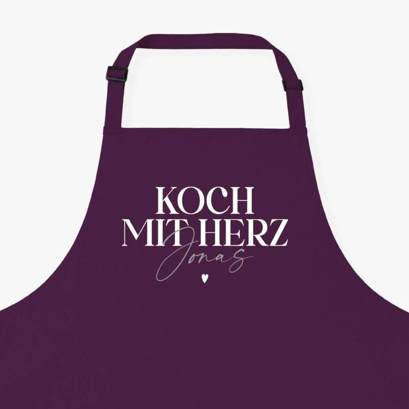 Purple apron with black buckle straps and white 'KOCH MIT HERZ' text on the front.