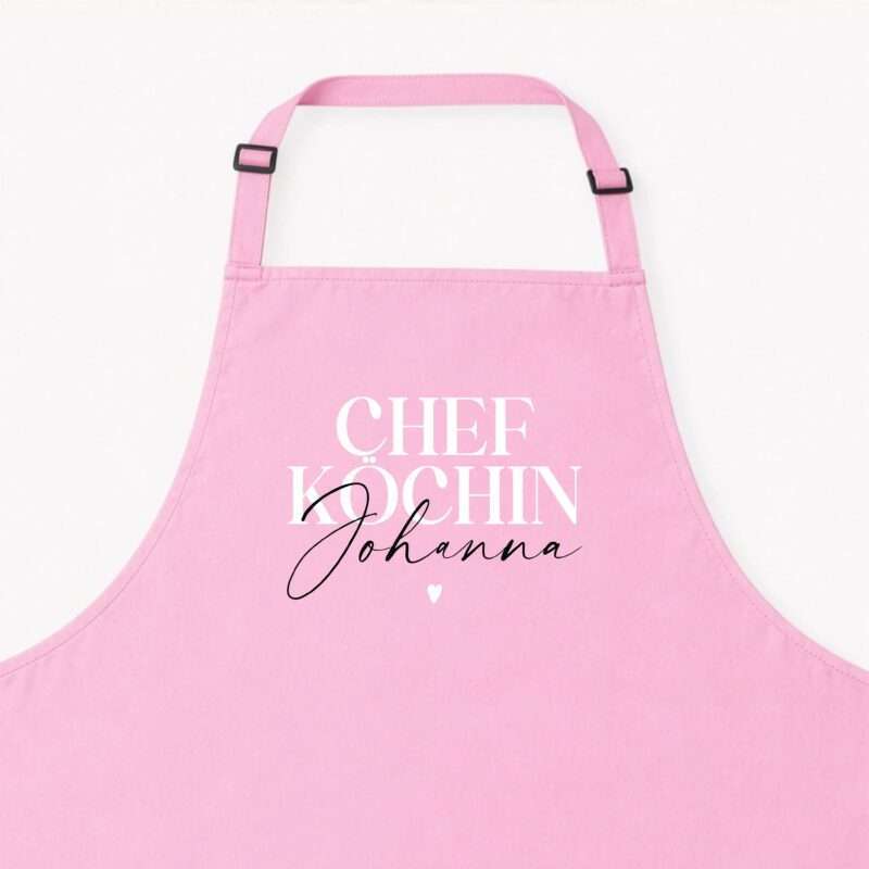 Close-up of a pink fabric bag or apron with adjustable shoulder straps and black buckles against a light background.
