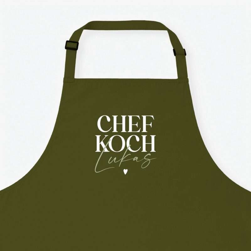 Olive-green apron front with buckle straps and large white text 'CHEF KOCH' across the chest, plus a cursive signature and heart motif.