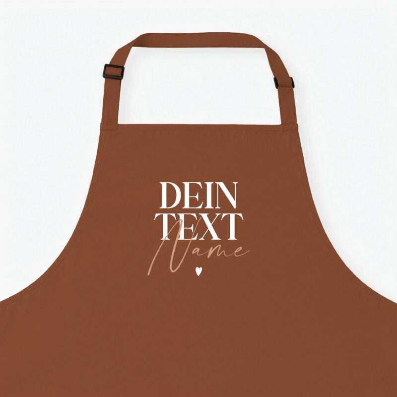 Close-up of a brown apron with straps and buckles against a light background, showing the top portion and stitching details, with partial text