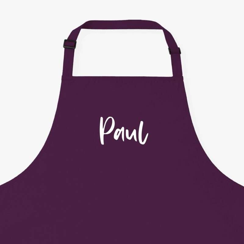 Close-up of a purple apron with an adjustable neck strap and buckle against a light background.
