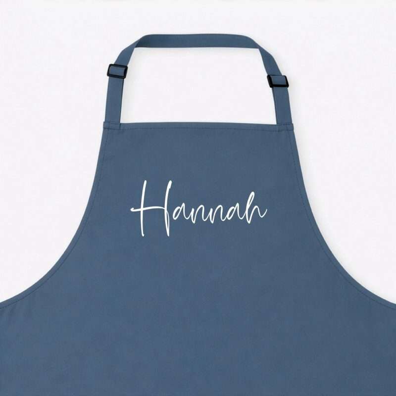 Blue apron with adjustable straps laid flat on a white background; partial cursive white text is visible on the front.