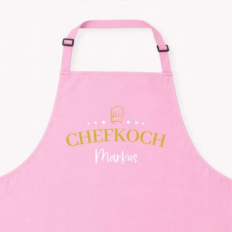 Close-up of a pink apron with a yellow chef hat graphic and white stars, text partially visible at bottom.