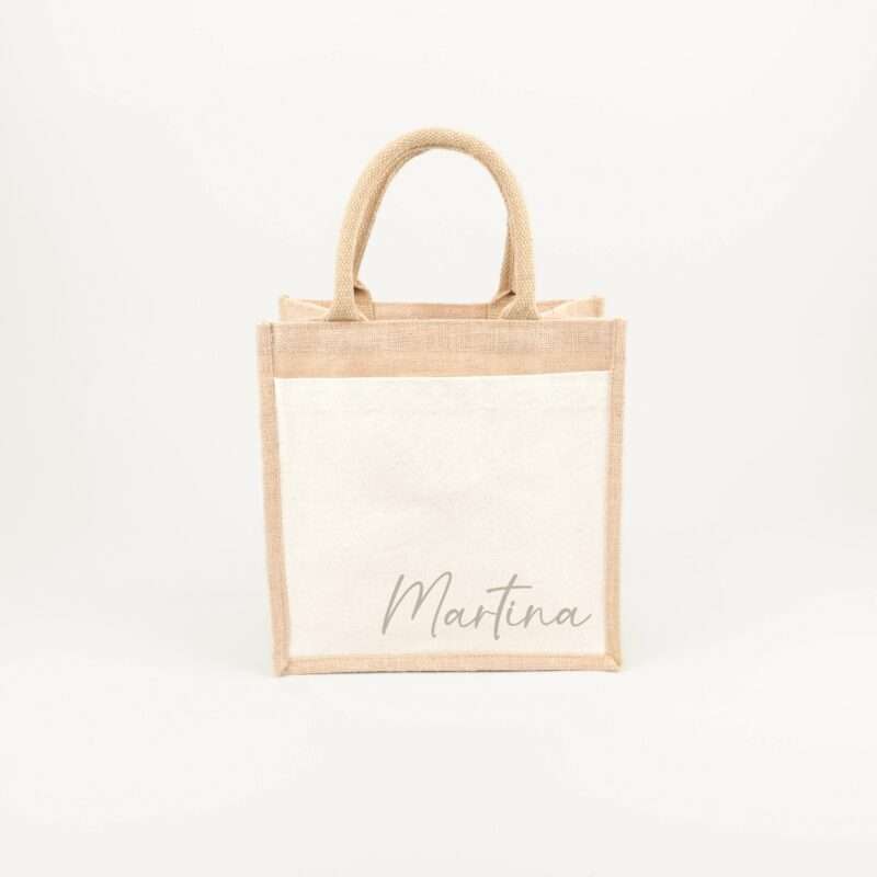 Beige burlap tote bag hanging by its handles against a pale background.