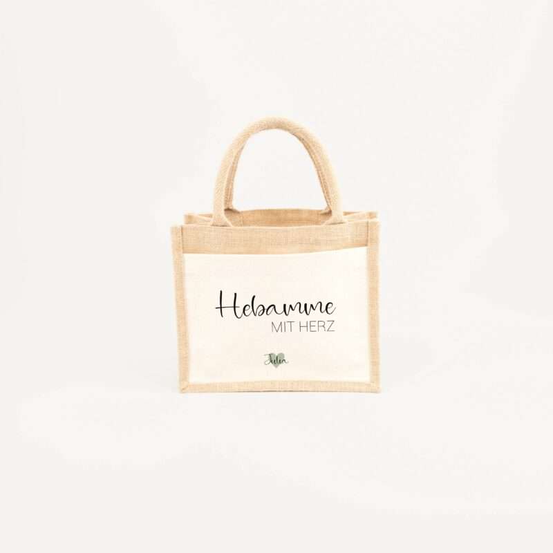 Beige jute tote bag with natural handles and a front panel showing the word 'Hebamme' and 'MIT HERZ' with a small 'Julia' signature.